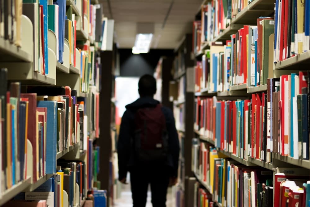 Una persona con mochila recorriendo los estantes de una biblioteca